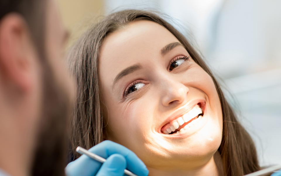 A woman smiling and looking toward a dentist, tools in hands