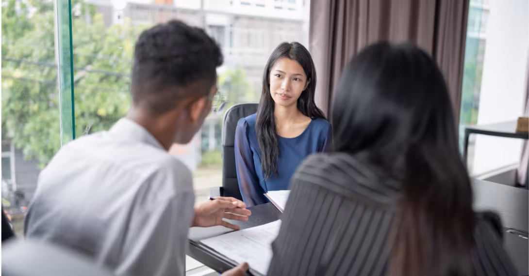 Three people discussing paperwork sitting around a desk